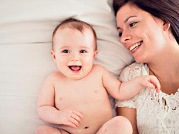 תינוקת שוכבת בגבה על המיטה וצוחקת כשאימה לצידה