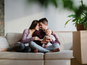 זוג יושב על הספה יחד עם התינוק שלהם, כשהם קרובים ומחייכים