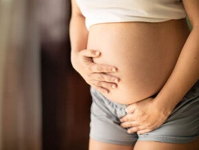 אישה בהריון מניחה את ידה על ביטנה החשופה ואת ידה השניה על המפשעה 