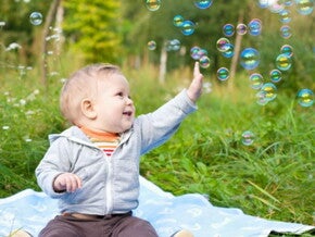 תינוק יושב ומרים ידו אל בועות סבון