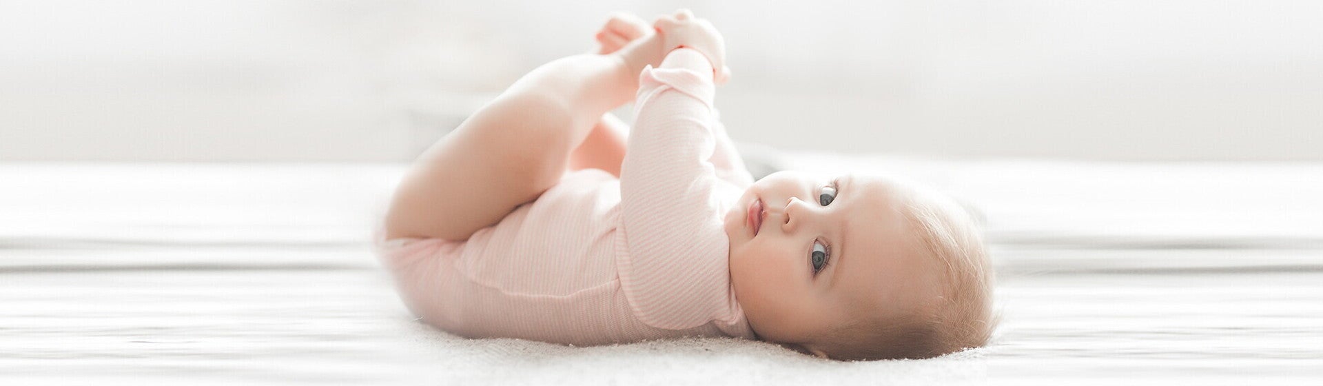 תינוק שוכב על גבו ומחזיק את רגליו בידיו