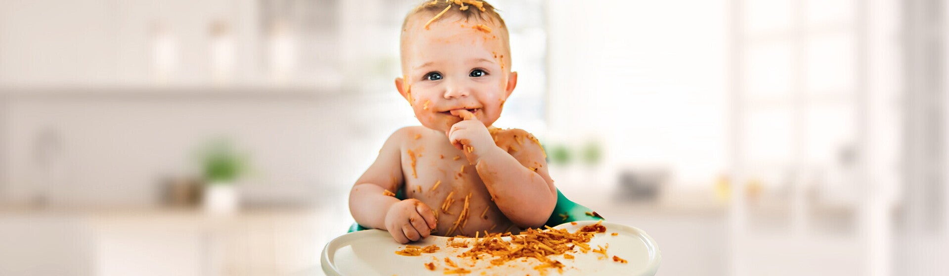 תינוק יושב בכסא האוכל שלו מלוכלך ברוטב אדום של פסטה